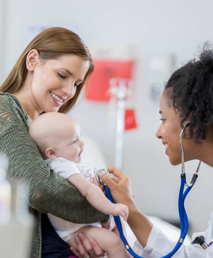 A mother holding a baby while a doctor uses a stethoscope on a baby for tablet