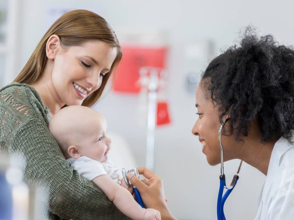 A mother holding a baby while a doctor uses a stethoscope on a baby